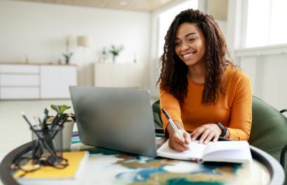 Image by Prostock-studio via Shutterstock. Woman sitting at desk working on laptop taking notes. Image by Prostock-studio via Shutterstock.
